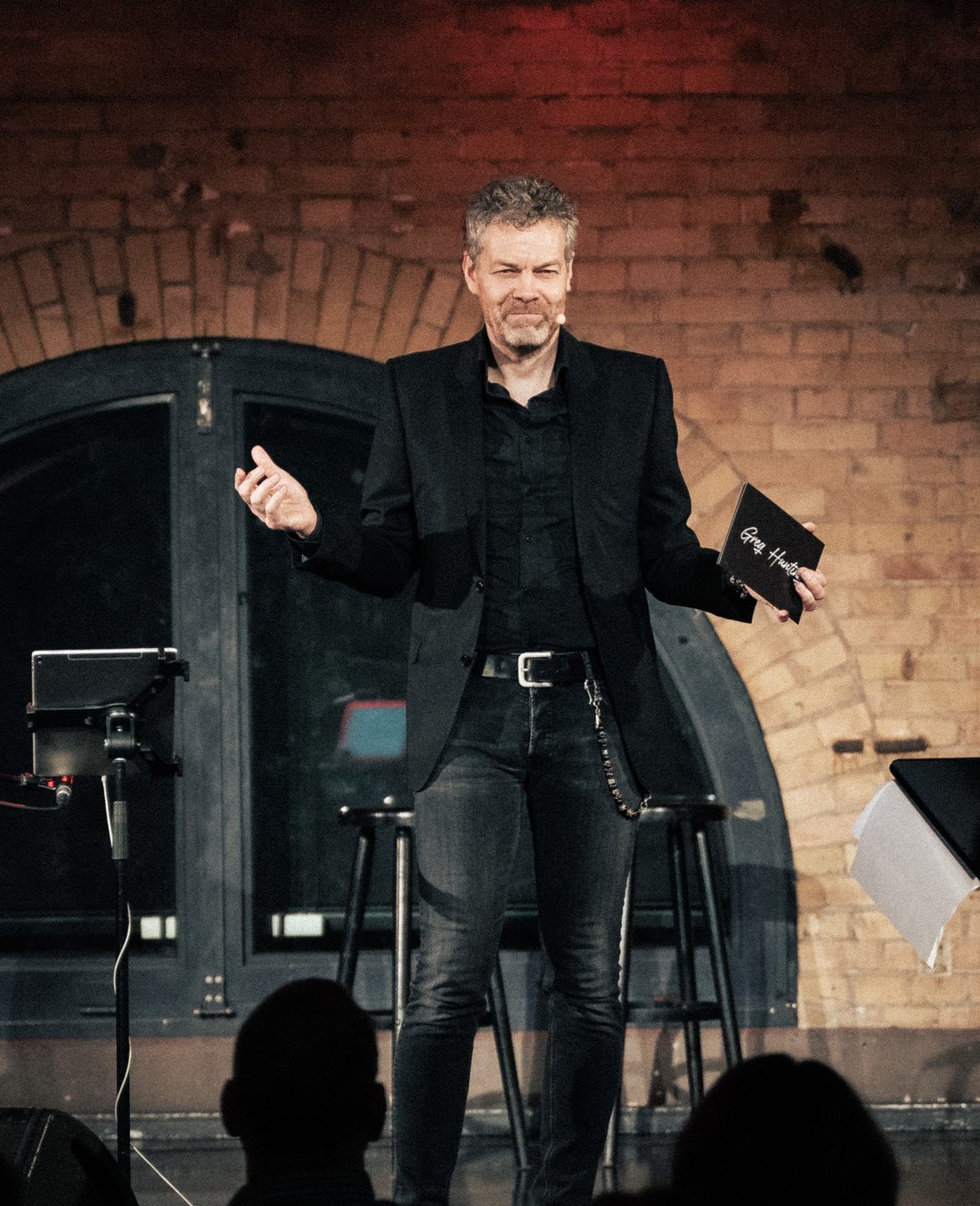 Greg Hunting spricht beim Coaching-Konzert mit offener Geste zum Publikum, das Greg-Hunting-Booklet in der Hand