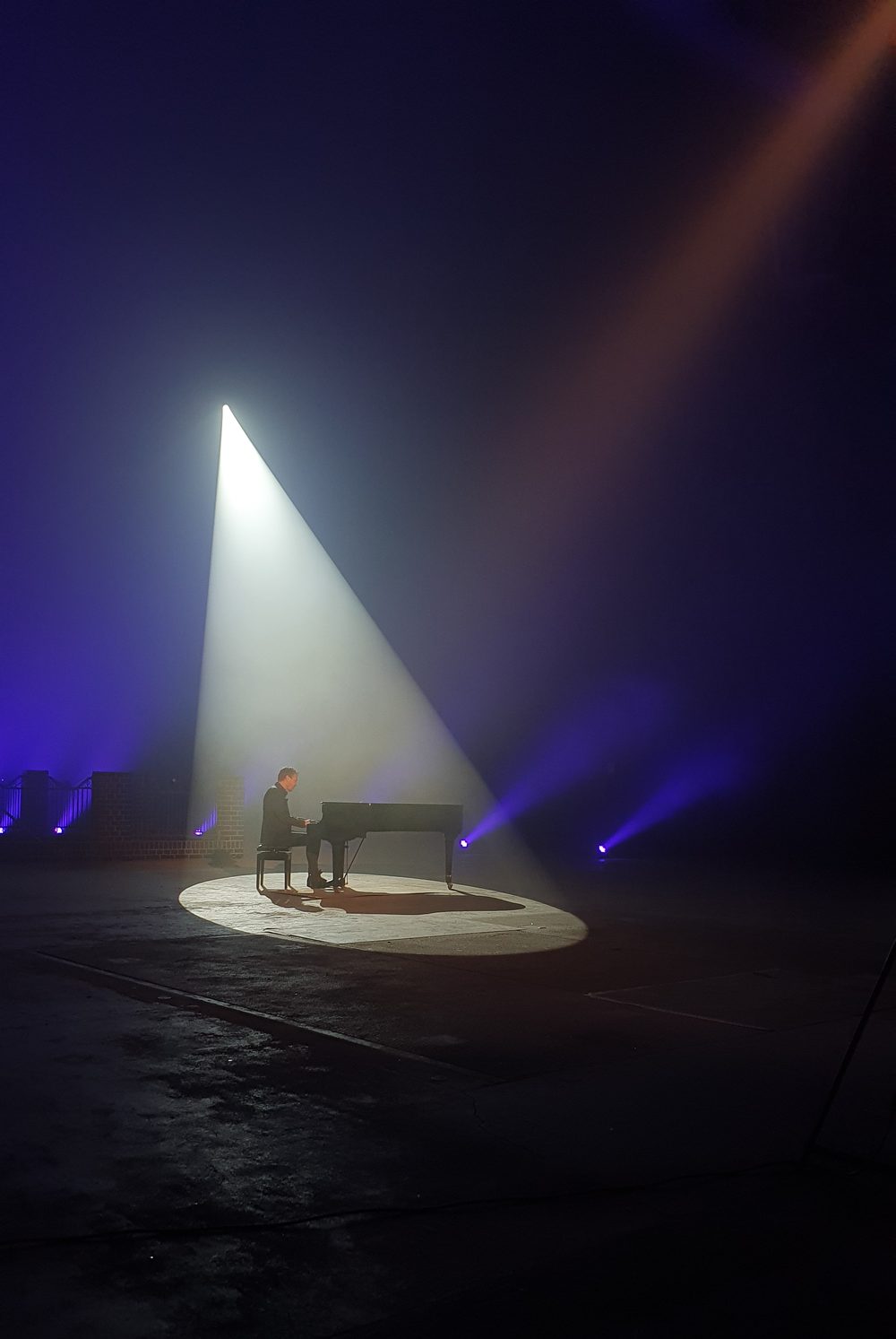 Greg Hunting am schwarzen Flügel unter einem dramatischen Lichtkegel, blauer Nebel im Raum